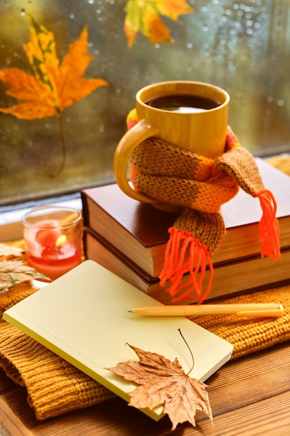 Cup of tea, autumn leaves, books, notebook and red knitted plaid on wooden table