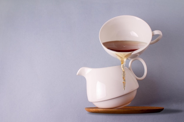 A cup of tea balances on a white ceramic teapot copy space