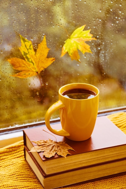 Cup of tea books autumn leaves and candle on window sill at home