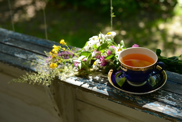 Cup of tea and bouquet chamomile flowers wildflowers on wooden table in garden blurred background