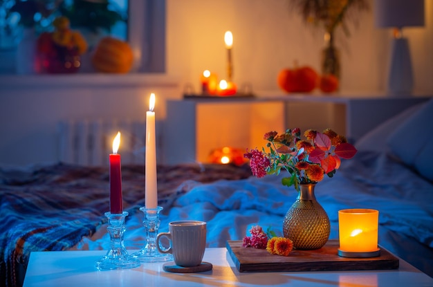 Cup of tea and chrysanthemum in vase with burning candles in bedroom