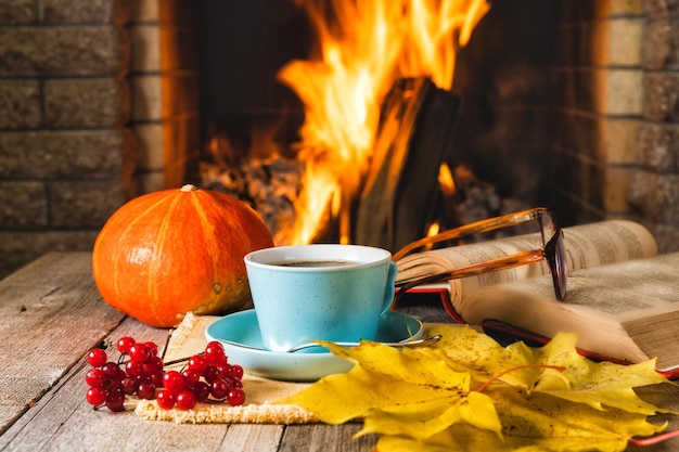 A cup of tea or coffee pumpkin autumn leaves and viburnum berries before cozy fireplace in country h...