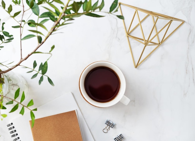 A cup of tea craft notepad and accessories on a light marble background with green branches closeup Spring women's concept Top view and copy space