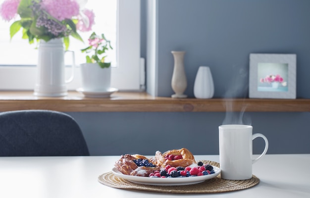 Cup of tea  and  danish with berries  on  white table