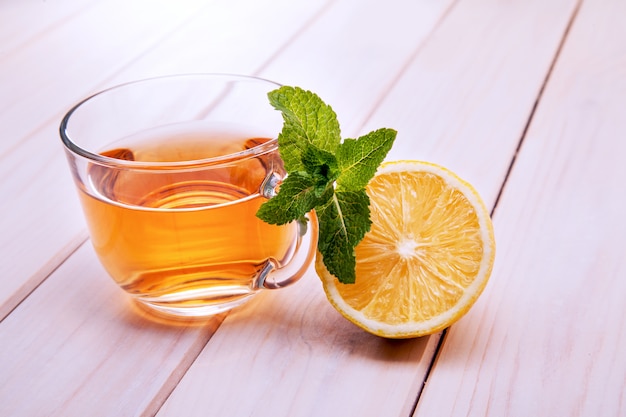 Cup of tea, glass teapot, mint and lemon on a wooden table