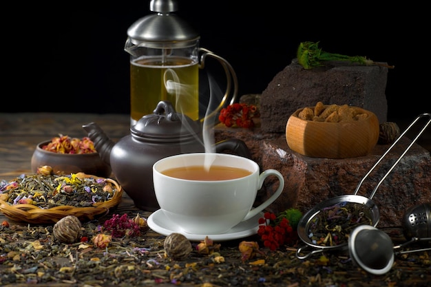 A cup of tea is surrounded by a teapot and a teapot with a bunch of fruits and nuts.