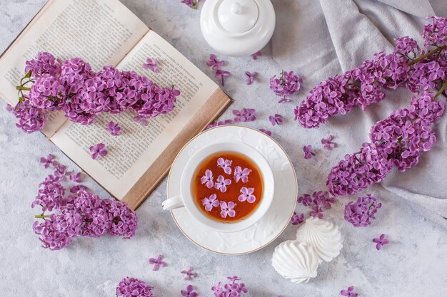 A Cup of tea, meringue, branches of blooming lilac and an old book