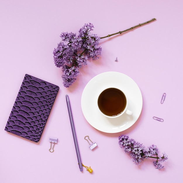 A cup of tea notebooks a pen a bouquet of lilacs on a purple background Purple spring flowers