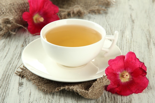 Cup of tea and pink mallow flowers on wooden background