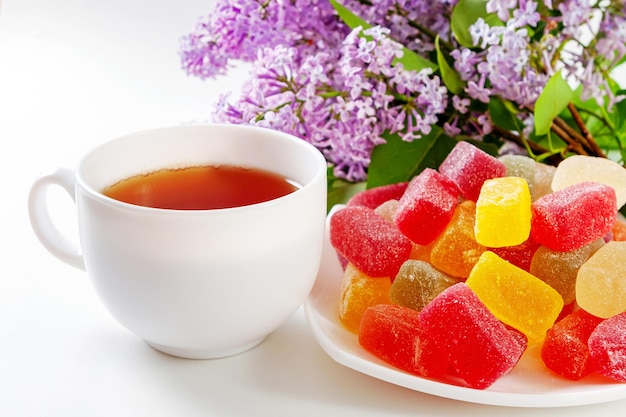 A cup of tea and a plate with sweets a bouquet of purple lilacs