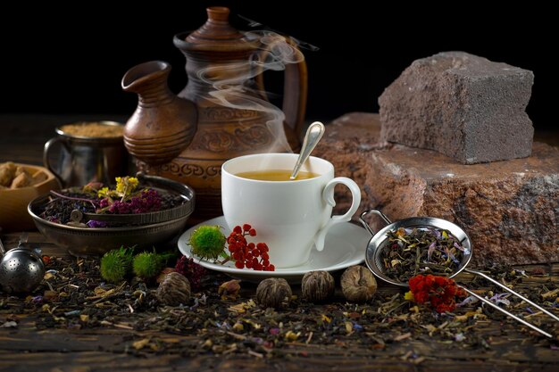 A cup of tea sits on a table with a teapot and a teapot with a flower arrangement.