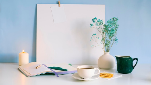 A cup of tea stands on white table with notebook pen burning candle Preparation for writing text