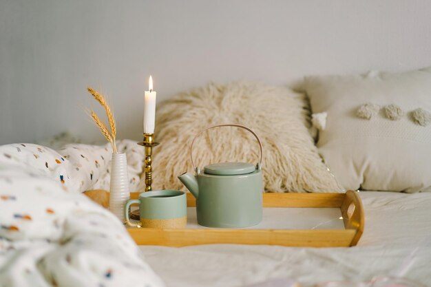 Cup of tea and teapot on a serving tray on a bed Breakfast in the bed in the morning The concept of enjoying tea at home spending time at home A cozy autumn or winter concept