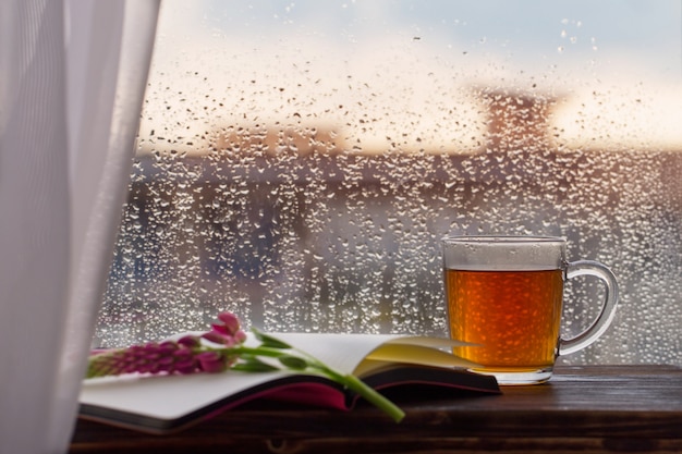 Cup of tea on  of  window with raindrops at sunset