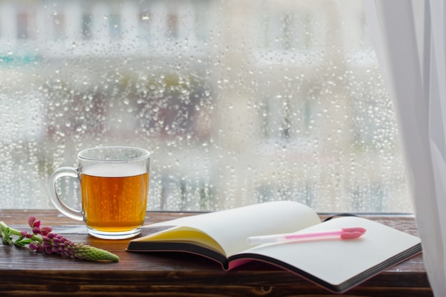 Cup of tea on  of  window with raindrops at sunset