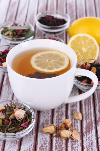 Cup of tea with aromatic dry tea in bowls on wooden background