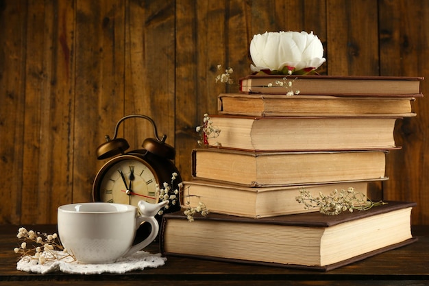 Cup of tea with books and clock on wooden background