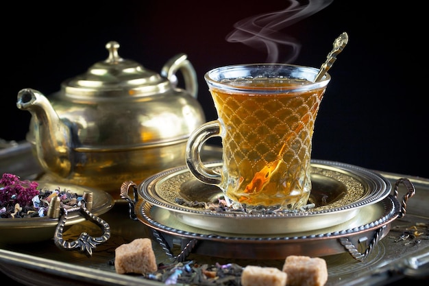 A cup of tea with a gold rim and a gold tray with teapots on it.