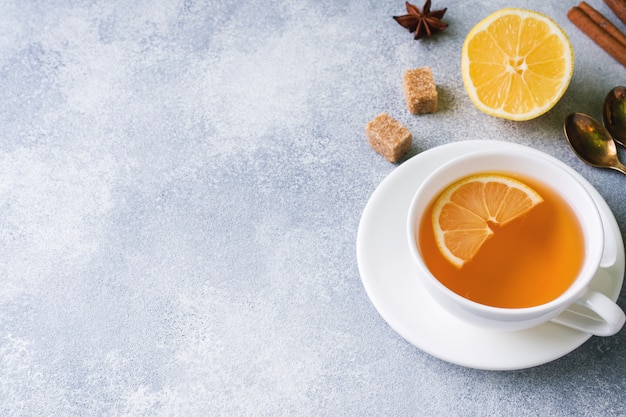 Cup of tea with lemon and brown sugar, cinnamon and anise on the table.