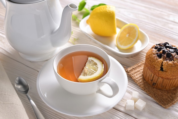 Cup of tea with lemon and cupcake on white table