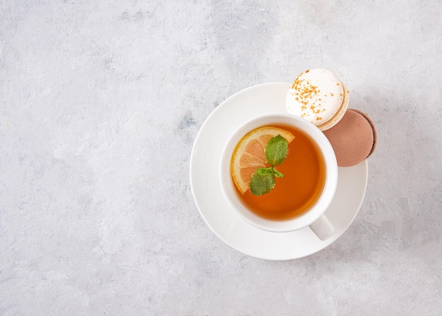 Cup of tea with lemon, mint and sweet macaroons  on a white textured background. Top view and copy space image