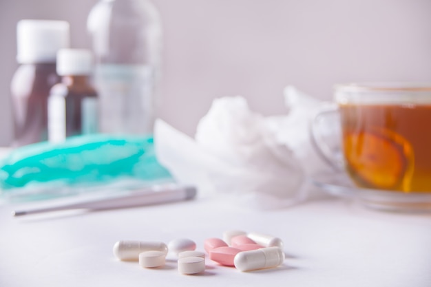 Cup of tea with lemon, thermometer, medicaments and pills on white table. Disease concept.