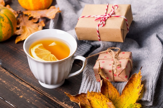 Cup of tea with lemon on wooden dark table with autumn leaves, pumpkins. Autumn decor, fall mood, autumn still life. Fall season concept. thanksgiving and halloween holiday. flat lay, copy space