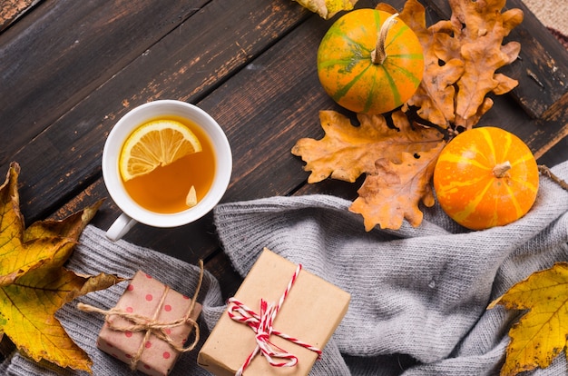 Cup of tea with lemon on wooden dark table with autumn leaves, pumpkins. Autumn decor, fall mood, autumn still life. Fall season concept. thanksgiving and halloween holiday. flat lay, copy space