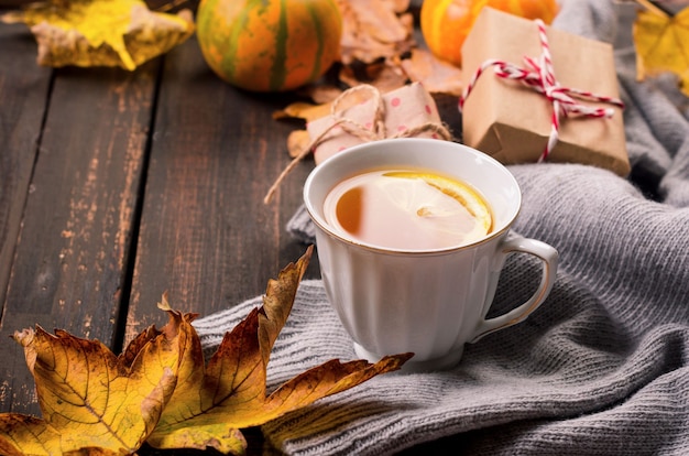 Cup of tea with lemon on wooden dark table with autumn leaves