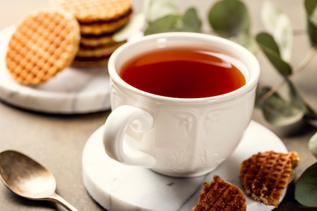 Cup of tea with mini stroopwafel, syrupwaffles cookies and eucalyptus twigs on light surface