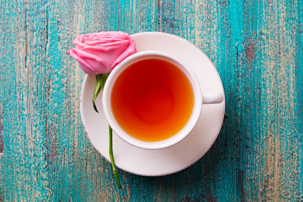 Cup of tea with pink rose Top view Copy space Colorful turquoise wooden background