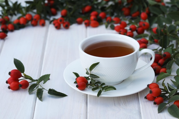 Cup of tea with rose berries on a white wooden background