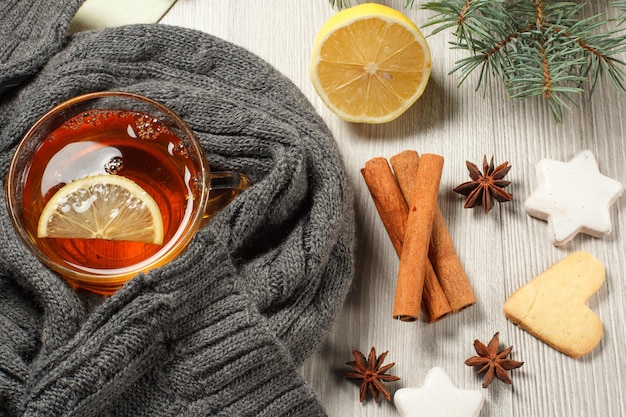 Cup of tea with slice of lemon wrapped up in wool scarf and gingerbread