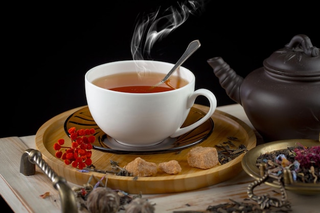 A cup of tea with a spoon in it and a black teapot on the table.