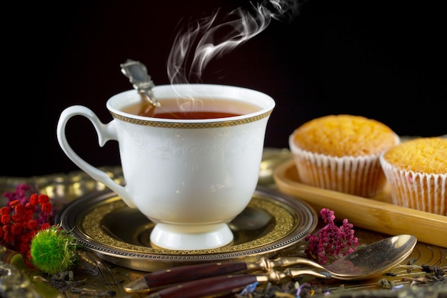 A cup of tea with a spoon in it and a muffin on a plate.