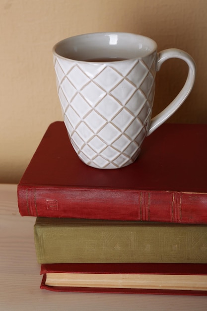 Cup of tea with stack of books on wooden table on light wall background