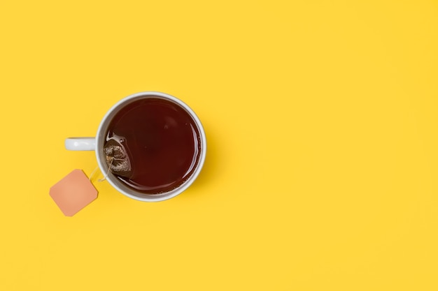 A cup of tea with a tea bag inside on a yellow background in a top view with copy space