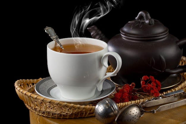 A cup of tea with a teapot and a pot of red flowers