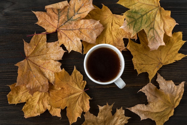 Cup of tea on wooden table with yellow autumn leaves around Hot tea amid autumn foliage