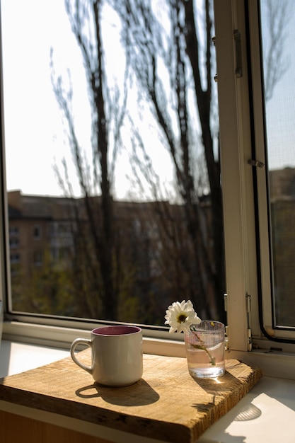 A cup of tea on a wooden tray is standing by the window