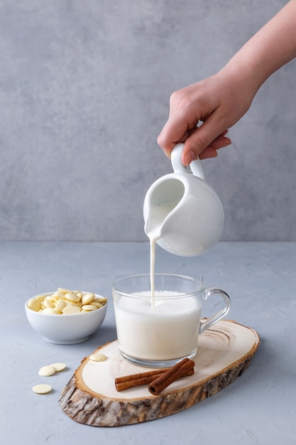 A cup of white hot chocolate and cinnamon on a wooden stand on a gray surface. Keto healthy breakfast concept. Pouring drinks.