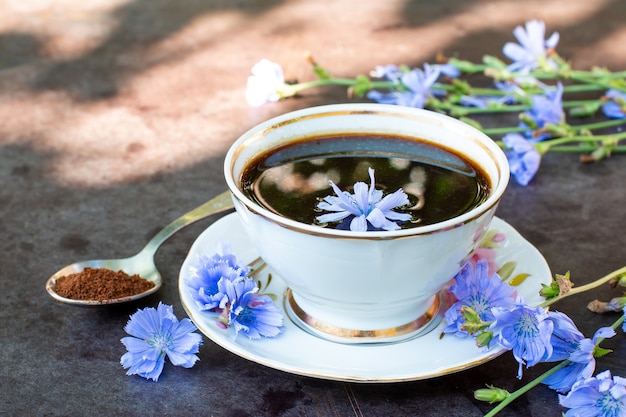 Cup with chicory drink and blue chicory flowers on table on the background of the garden. Herbal beverage. Selective focus