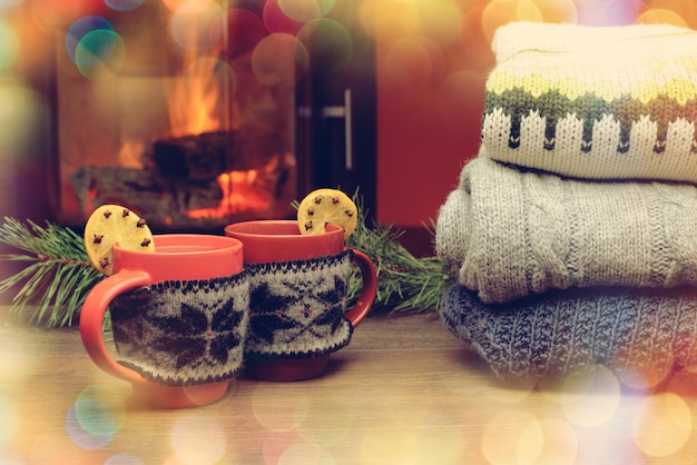 Cup with Christmas ornament near fireplace Mug in red knitted mitten standing near fireside