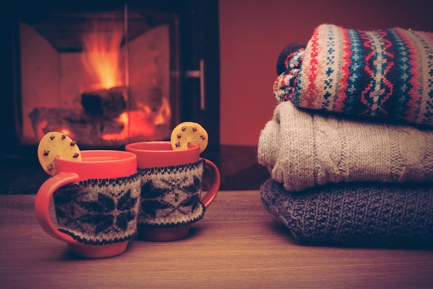 Cup with Christmas ornament near fireplace Mug in red knitted mitten standing near fireside