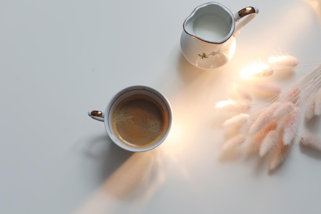 Cup with coffee and milk jug on a white wooden background closeup Energy breakfast morning routine concept