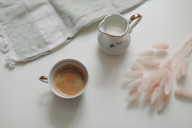 Cup with coffee and milk jug on a white wooden background closeup Energy breakfast morning routine concept