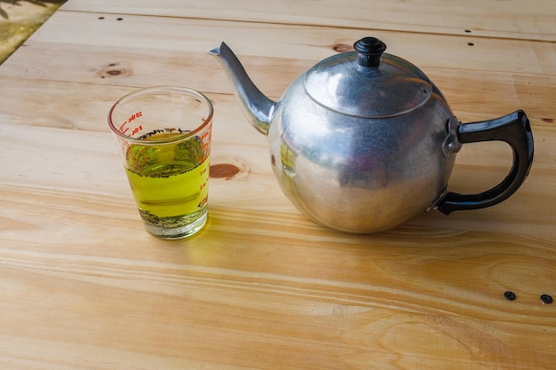 A cup with green tea and teapot on white wooden table background