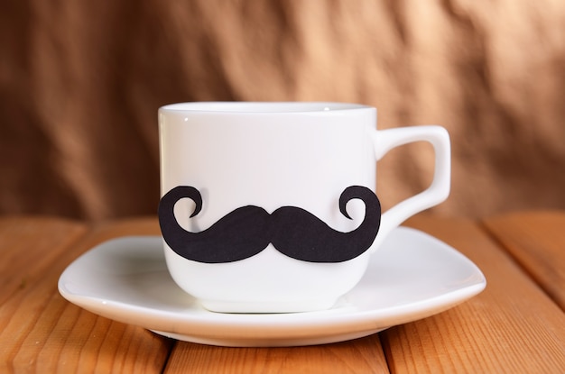 Cup with mustache on table on brown surface