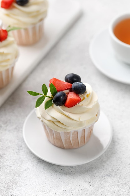 Cupcake with fresh berries vanilla cream green leaves on grey background Homemade dessert