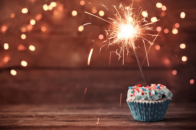 Cupcake with sparkler on old wooden background